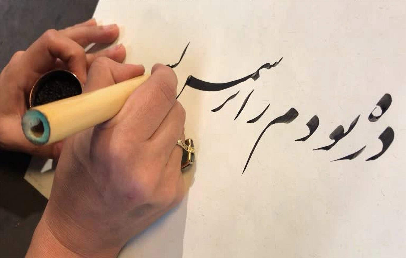 close-up of a woman’s hand writing in Persian calligraphy (Nastaliq)
